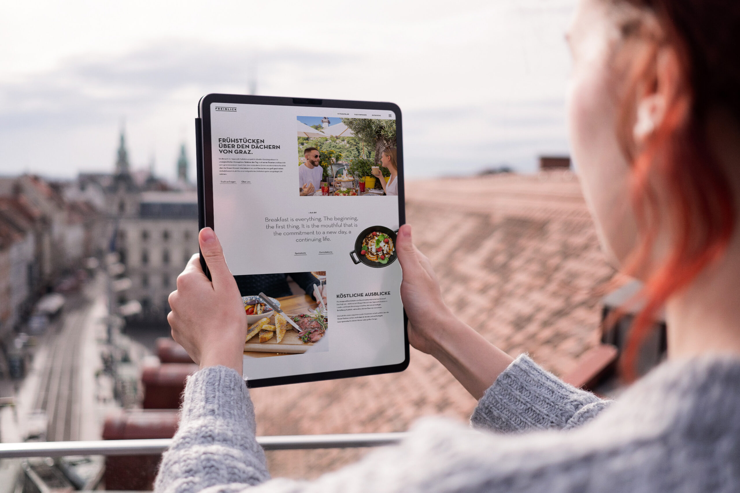 A woman holding an ipad tablet with a city view at a Freiblick cafe.