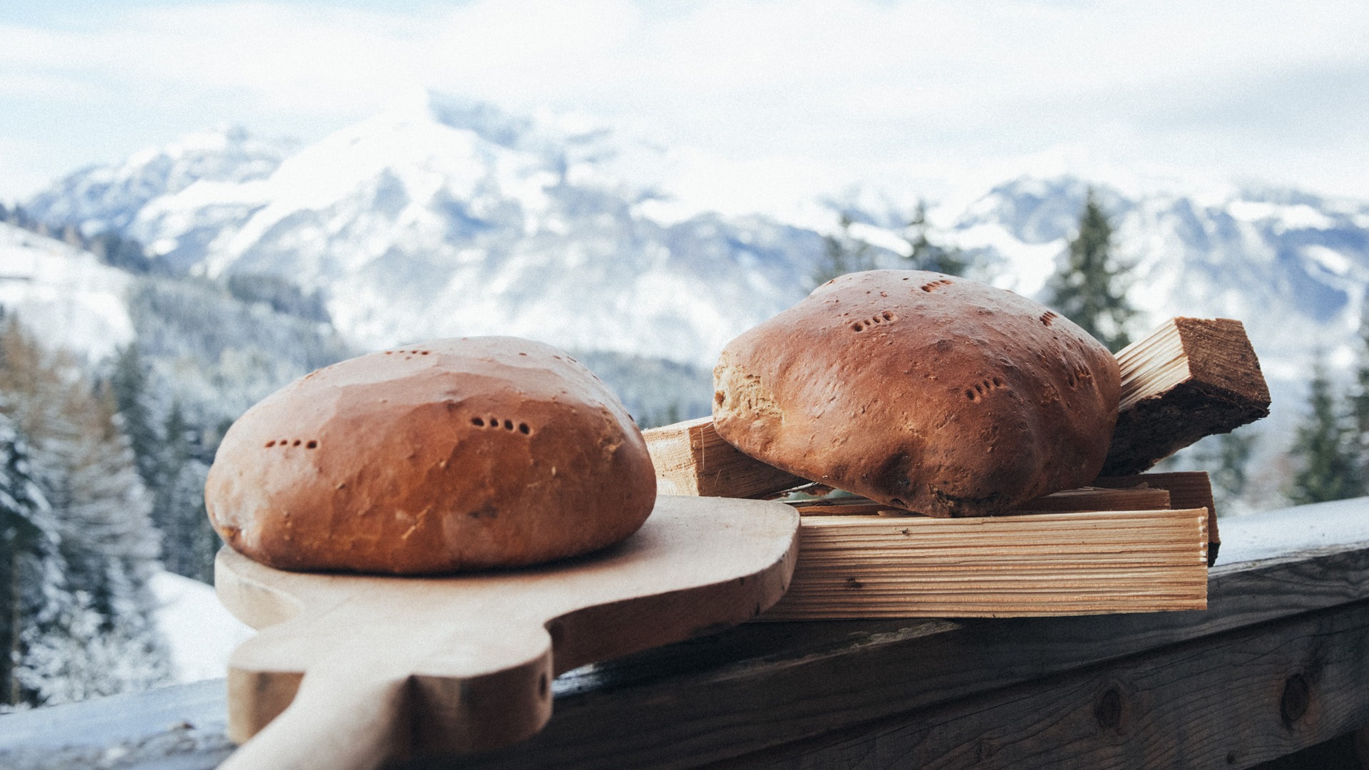 Two loaves of bread on a wooden board with mountains in the background at Eggenhof.