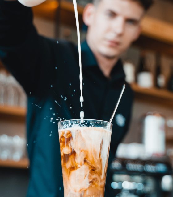 A barista pouring milk into an iced coffee.