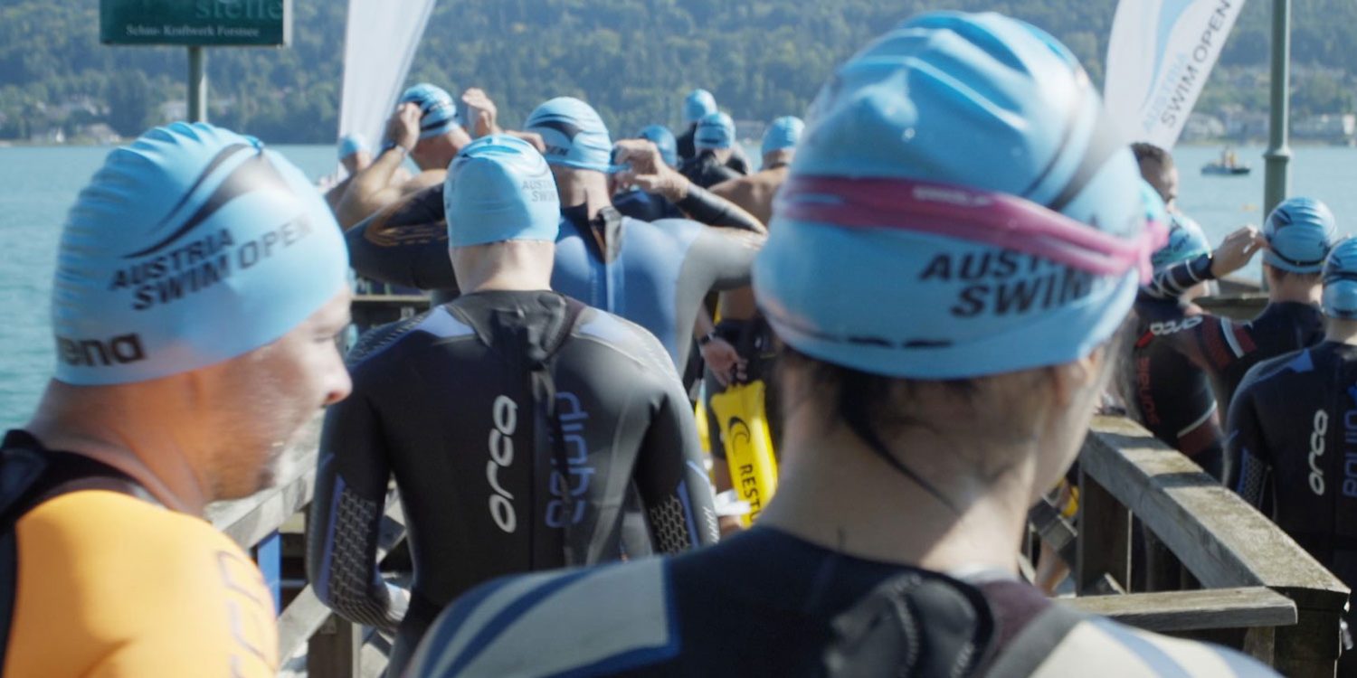 A group of swimmers in wetsuits standing on a dock at the Austria Swim Open.