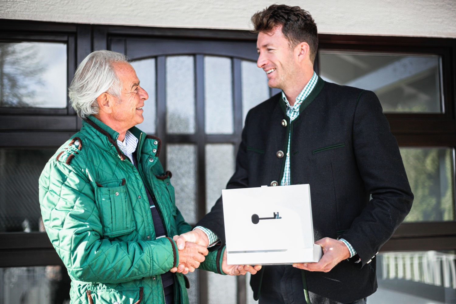 A man shaking hands with an older man holding a box at Gersin Immobilien.