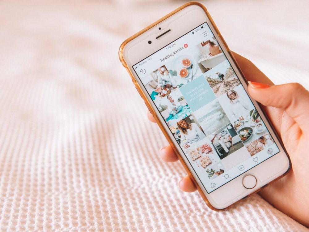 Eine Person hält ein iPhone mit Bildern darauf und präsentiert Designideen für die Planung und Erstellung eines ästhetisch ansprechenden Instagram-Feeds.