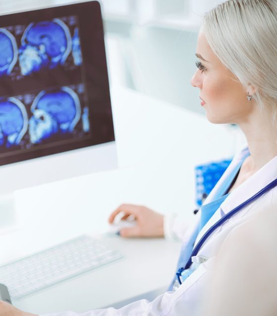 A female doctor is analyzing an MRI image using a computer.