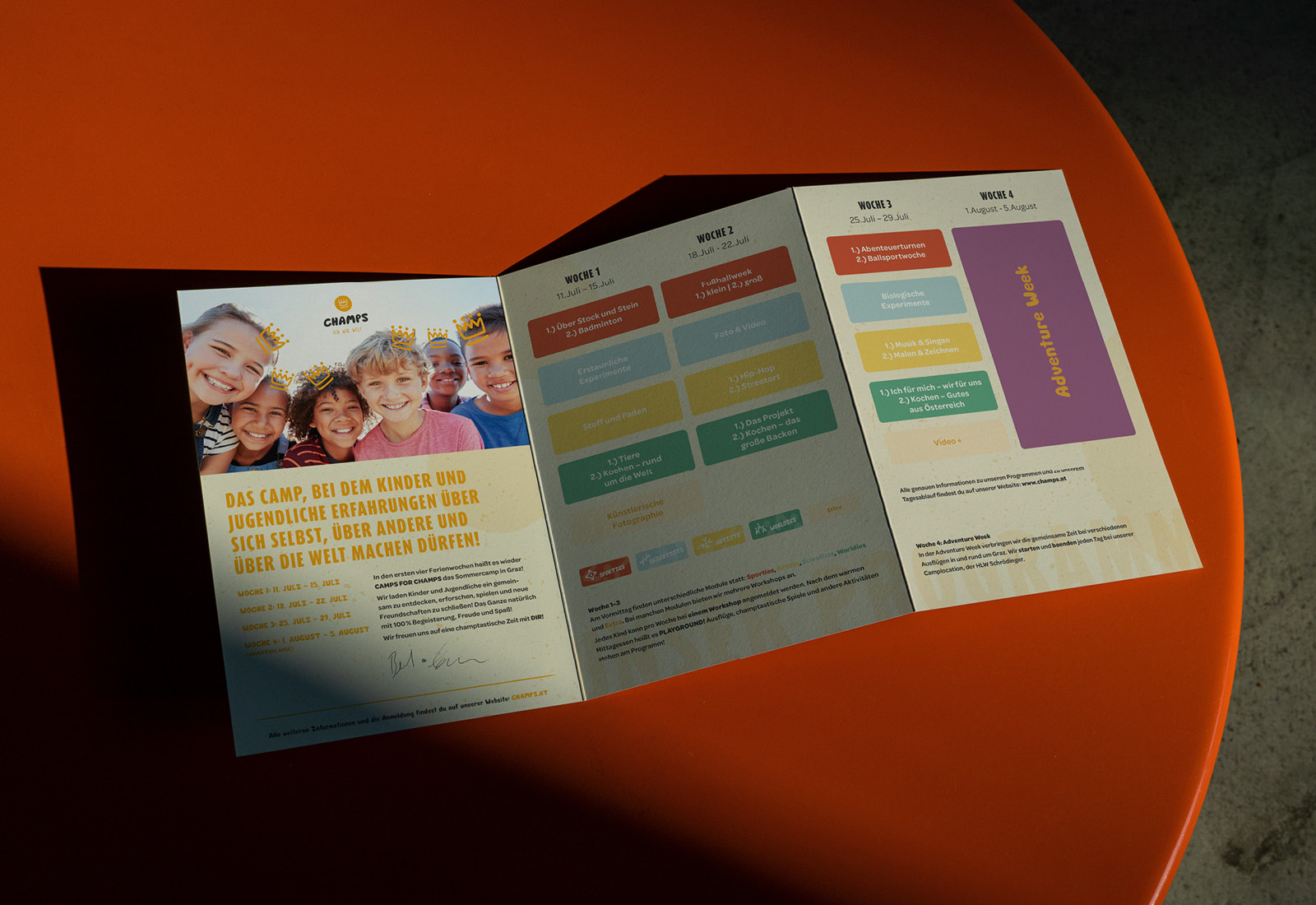 Eine dreifach gefaltete Broschüre, die Champs zeigt und Kinder zeigt, die auf einem orangefarbenen Tisch sitzen.