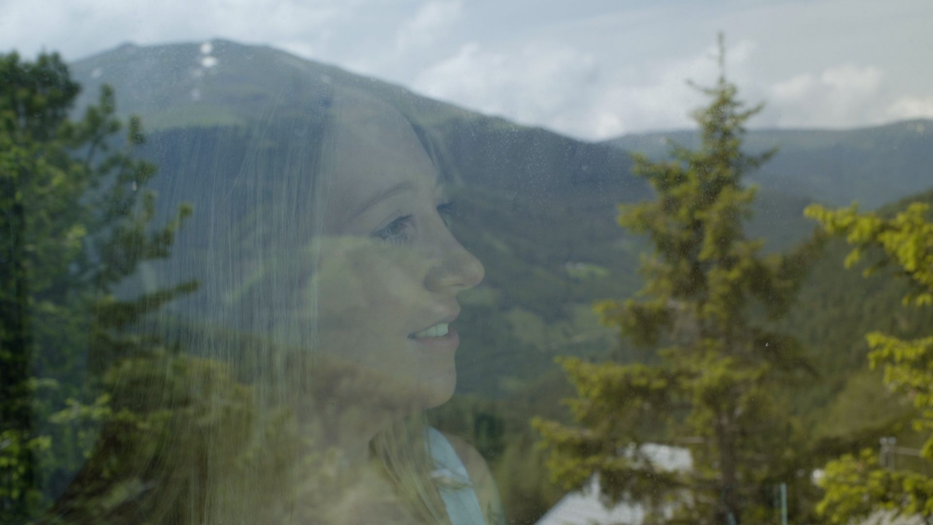 Eine Frau schaut aus einem Fenster in die Alpen.