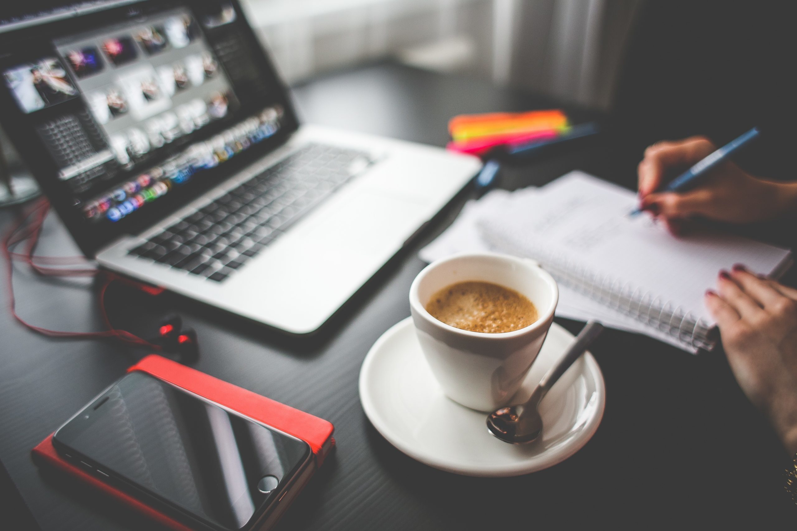 Eine Frau sitzt mit einer Tasse Kaffee und einem Notebook an einem Schreibtisch und arbeitet online.