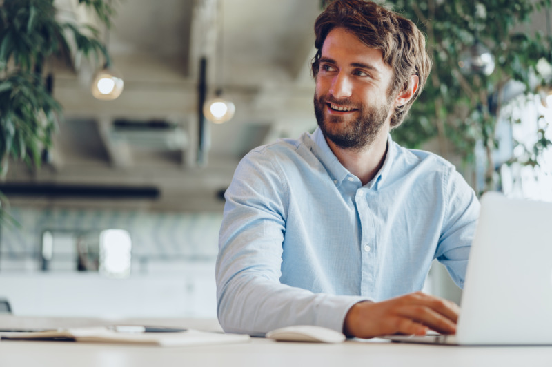 A smiling man using a laptop in an office while working on Mission Zero.