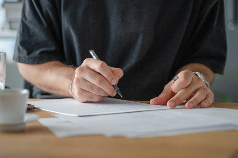 Ein Mann schreibt mit einem Stift auf ein Blatt Papier.