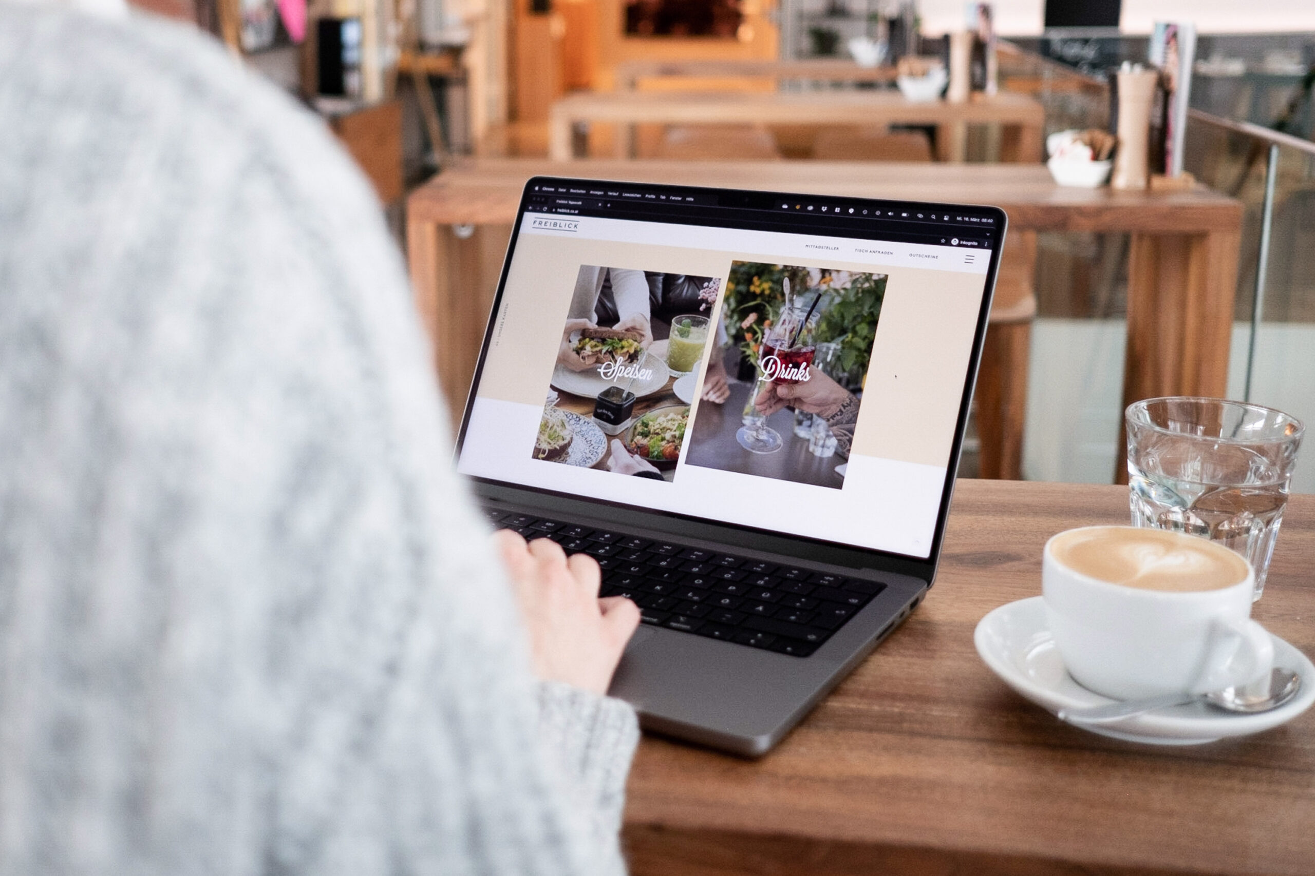 Eine Frau sitzt mit einem Laptop auf einem Tisch und trinkt eine Tasse Kaffee im Tagescafé.