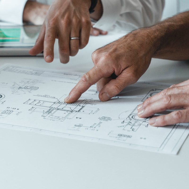Two people pointing at blueprints on a table.