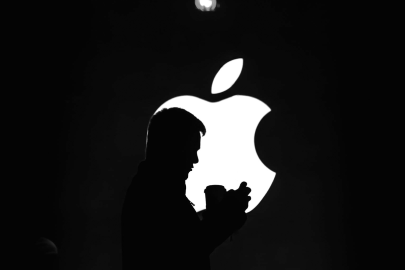 Die Silhouette eines Mannes, der ein Mobiltelefon vor einem Apple-Logo hält, das das Branding veranschaulicht.