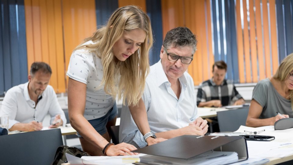 Eine Gruppe von Menschen sitzt während Boote Kamper an einem Schreibtisch in einem Klassenzimmer.