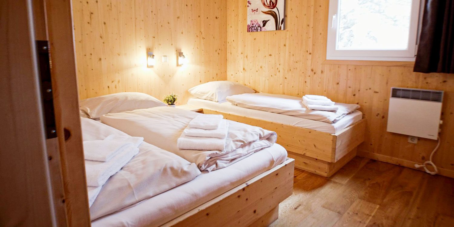 Two beds in a room at Alps Residence with wooden walls.