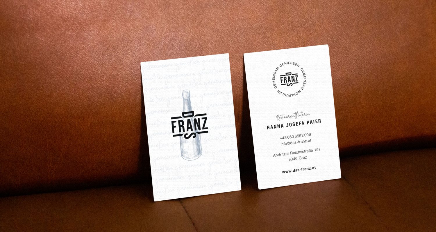 Zwei Das Franz-Visitenkarten auf einer Ledercouch.