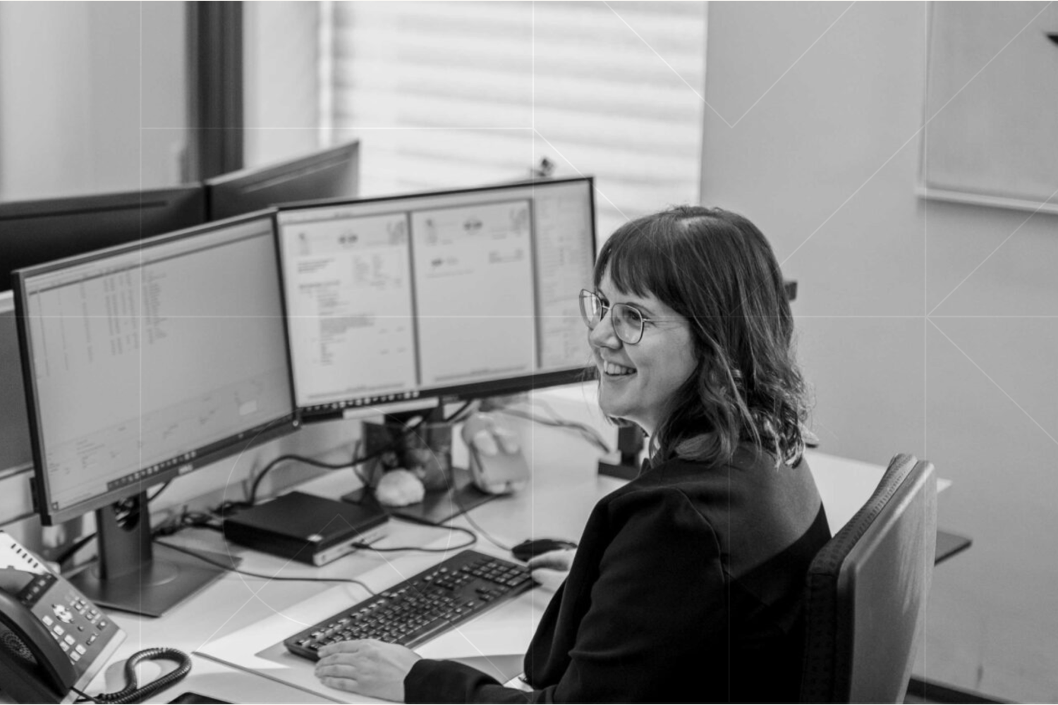 A woman managing tasks at a desk with two monitors.