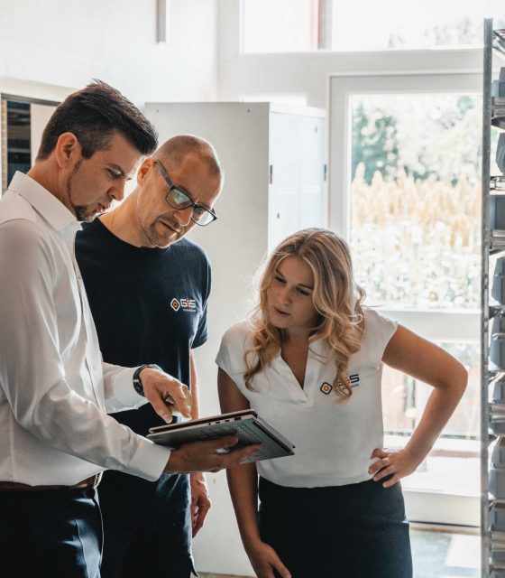 Three people standing in a kitchen looking at a tablet.