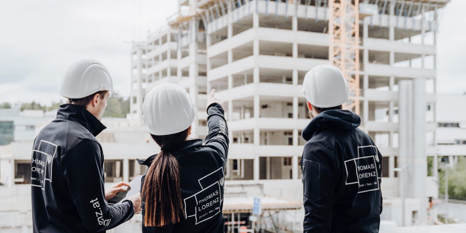 Three construction workers standing on a roof overlooking a construction site with the keyword "construction site.