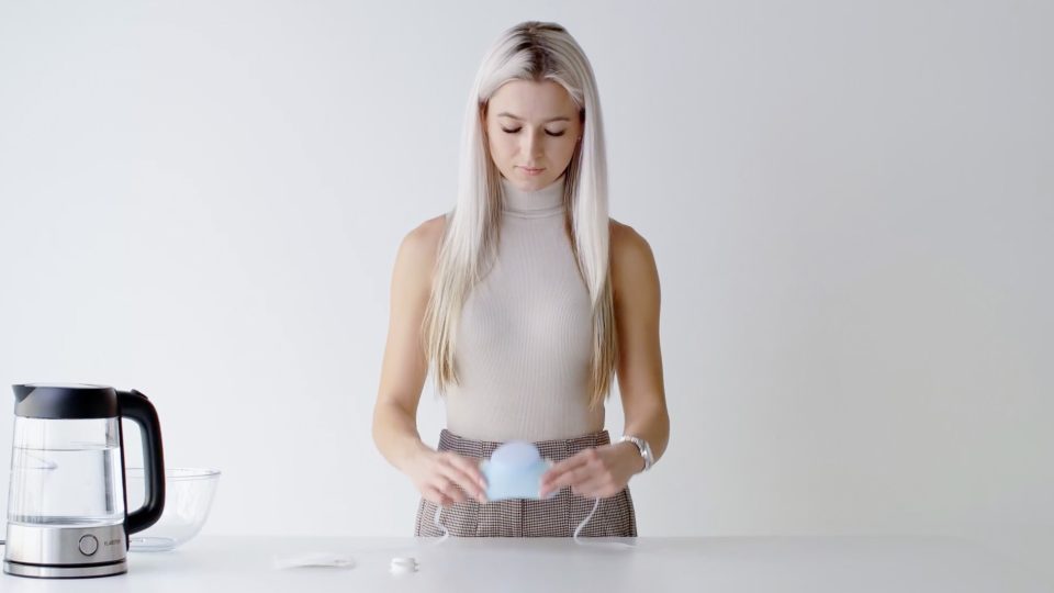 Eine junge Frau hält eine Tasse Tee vor einen Wasserkocher und sorgt so für Hygge-Atmosphäre.