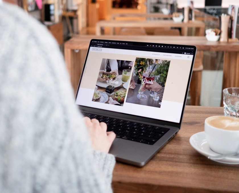 Eine Frau sitzt mit einem Laptop auf einem Tisch und trinkt eine Tasse Kaffee im Tagescafé.