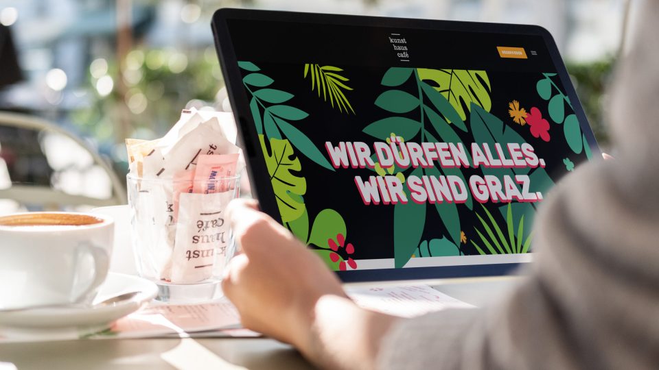 Eine Person sitzt mit einem Laptop und einer Tasse Kaffee an einem Tisch im Kunsthauscafé.