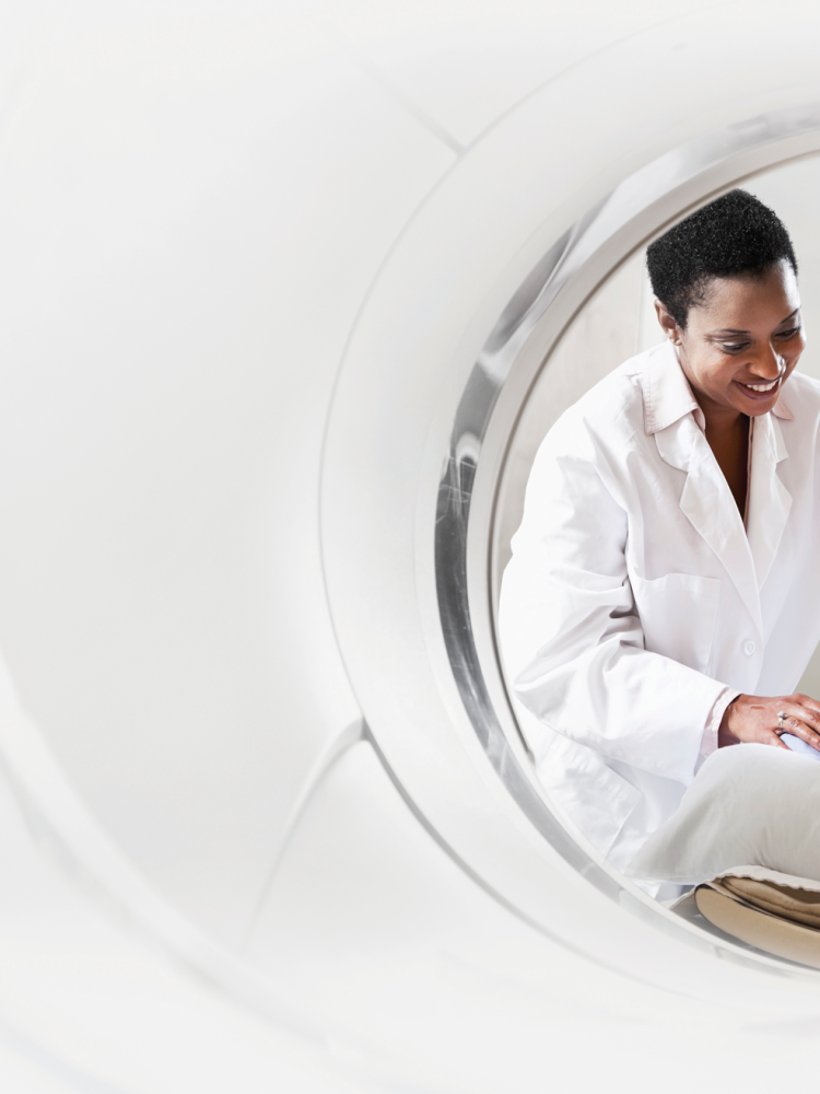 A woman in a white coat is looking at a mri machine.