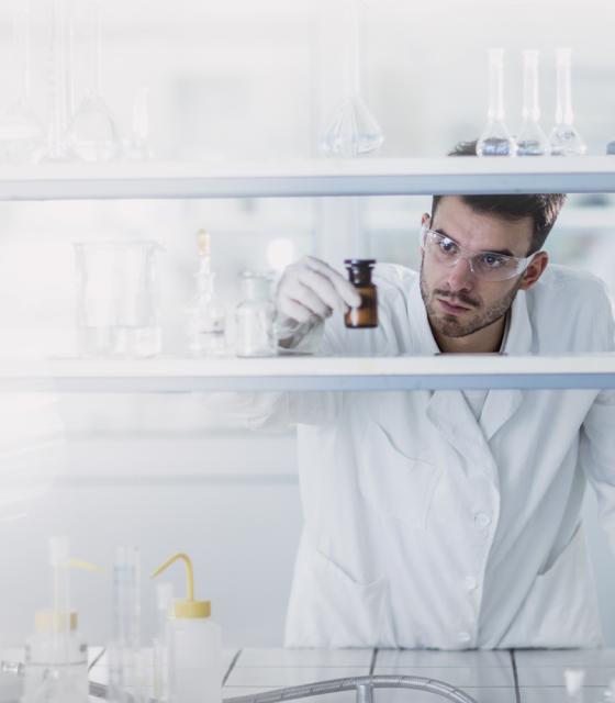 A man in a lab coat is looking at a bottle.